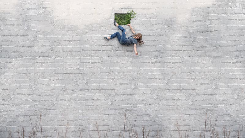 a large white brick wall, with a small window out of which a dancer appears to be either falling or hanging
